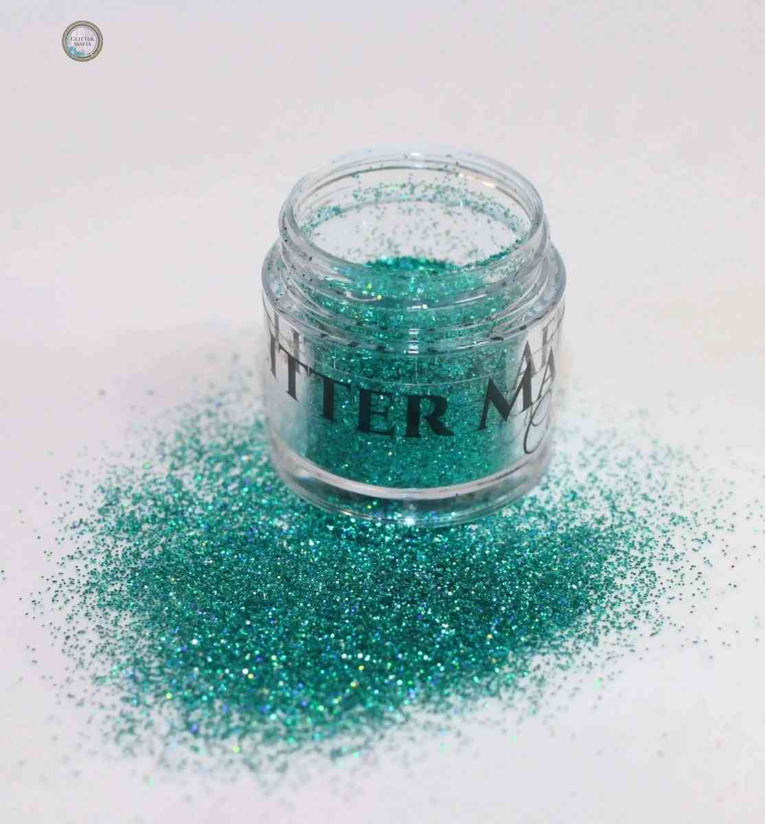 Glitter Mafia Flaunt Loose Glitter in teal shade spilled from small clear jar on white surface