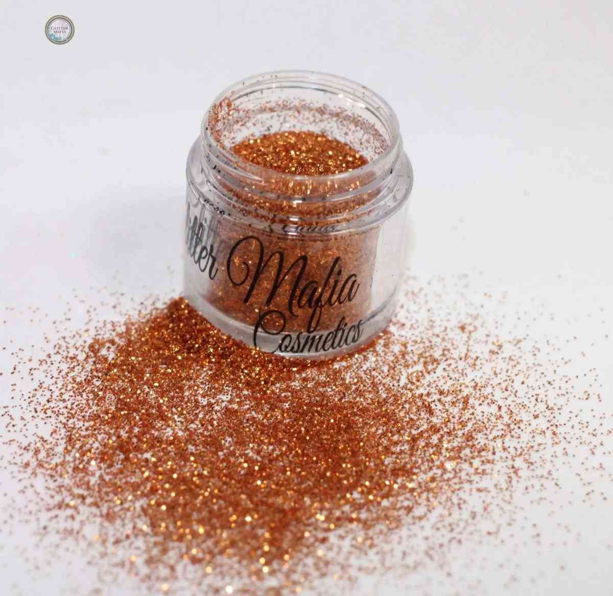 Glitter Mafia Marigold Pressed Glitter in clear jar with bright orange sparkling glitter spilled on white surface