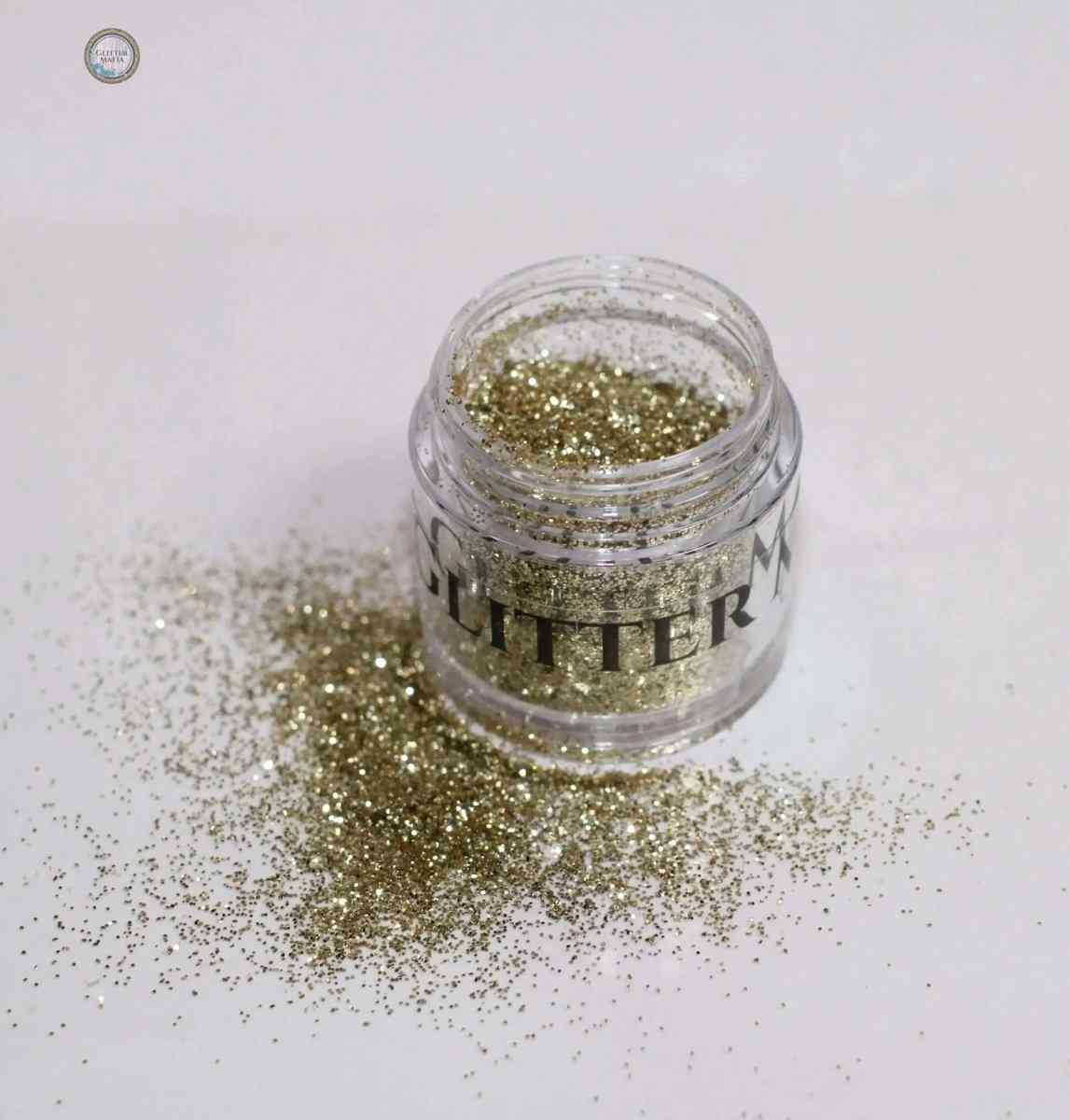 Glitter Mafia 24k Gold Malibu Loose Glitter in a clear jar with spilled glitter on white surface