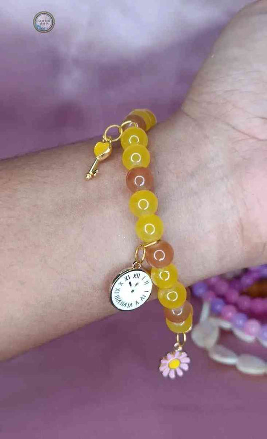 Glitter Mafia mustard charm bracelet with yellow and brown beads and clock and flower charms on wrist