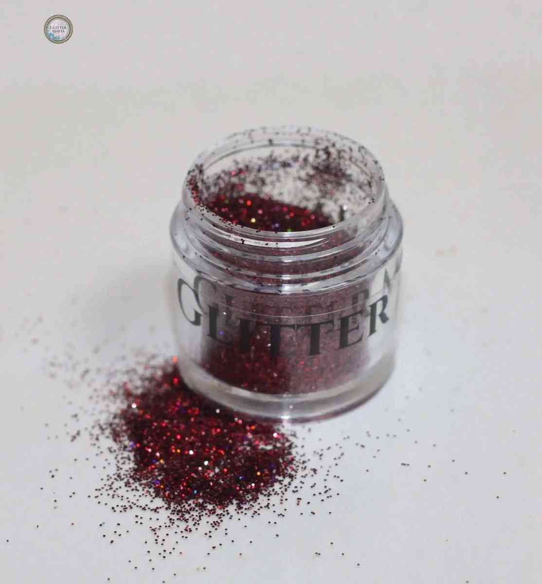 Glitter Mafia 24k gold dazzling loose glitter in an open jar with spilled glitter on white surface