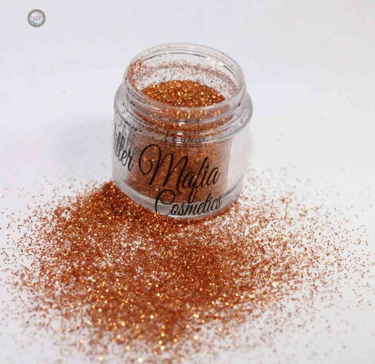 Glitter Mafia Marigold Pressed Glitter in clear jar with bright orange sparkling glitter spilled on white surface